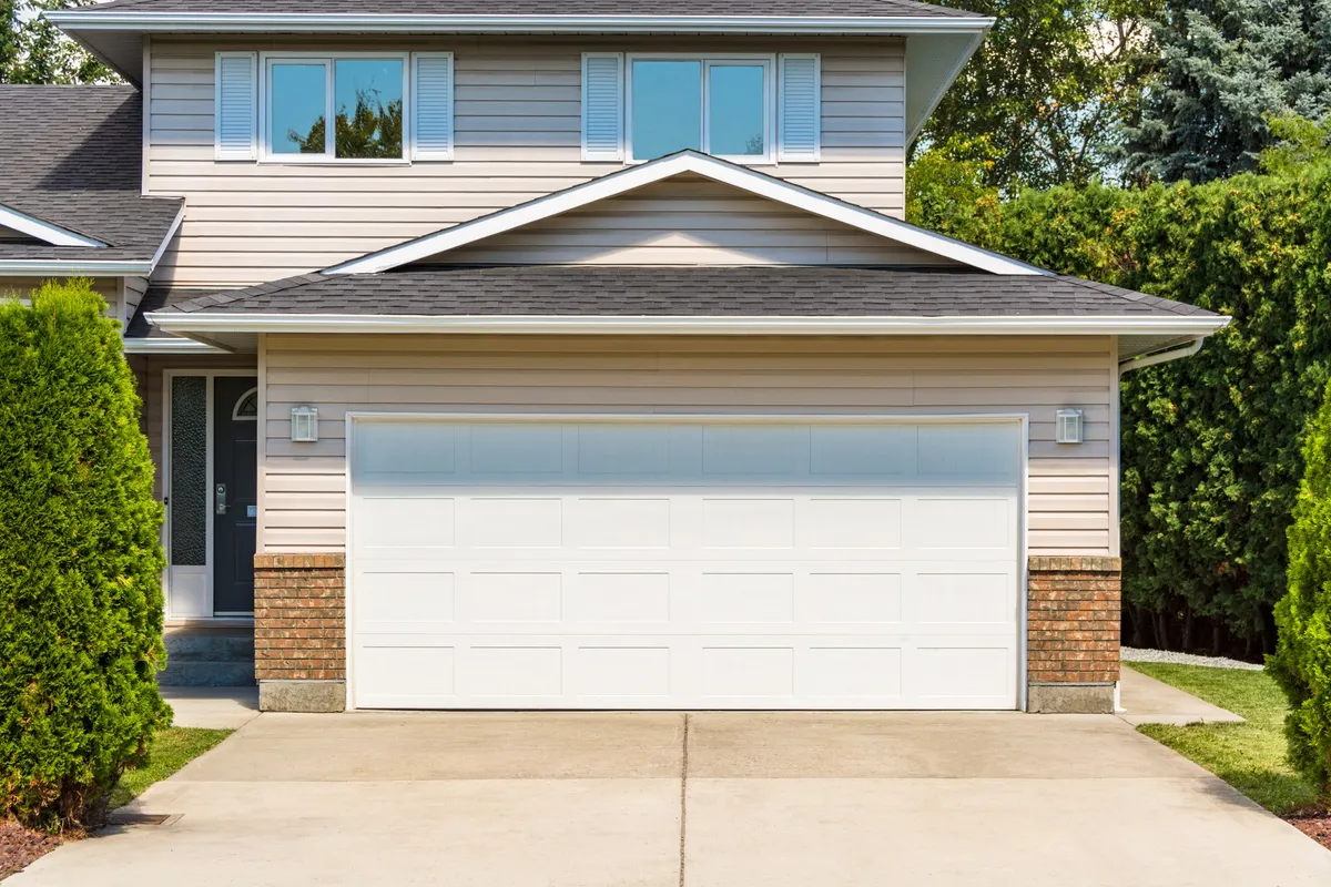 A wide garage door of a residential house with a concrete driveway, illustrating signs of potential repair needs.